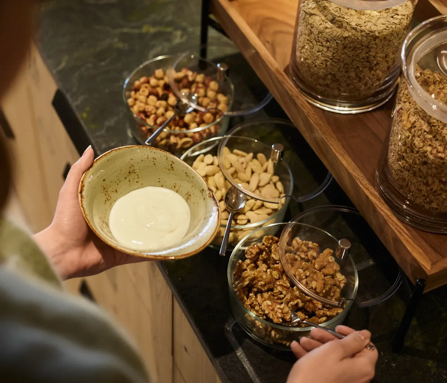 Al buffet della colazione dell’hotel AUI, una ragazza prepara una bowl di yogurt scegliendo tra una varietà di frutta secca e cereali per i suoi topping.