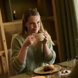 Una donna gusta un cappuccino seduta al tavolo dell’Hotel AUI, immersa in un’atmosfera accogliente.
