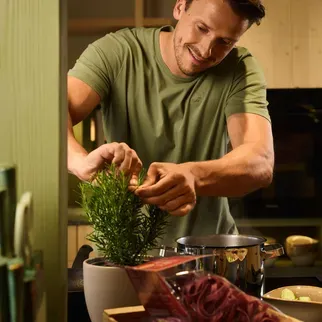 Un uomo con una maglietta verde si trova nella cucina comune dell’hotel AUI, mentre prepara del cibo sul piano di lavoro.