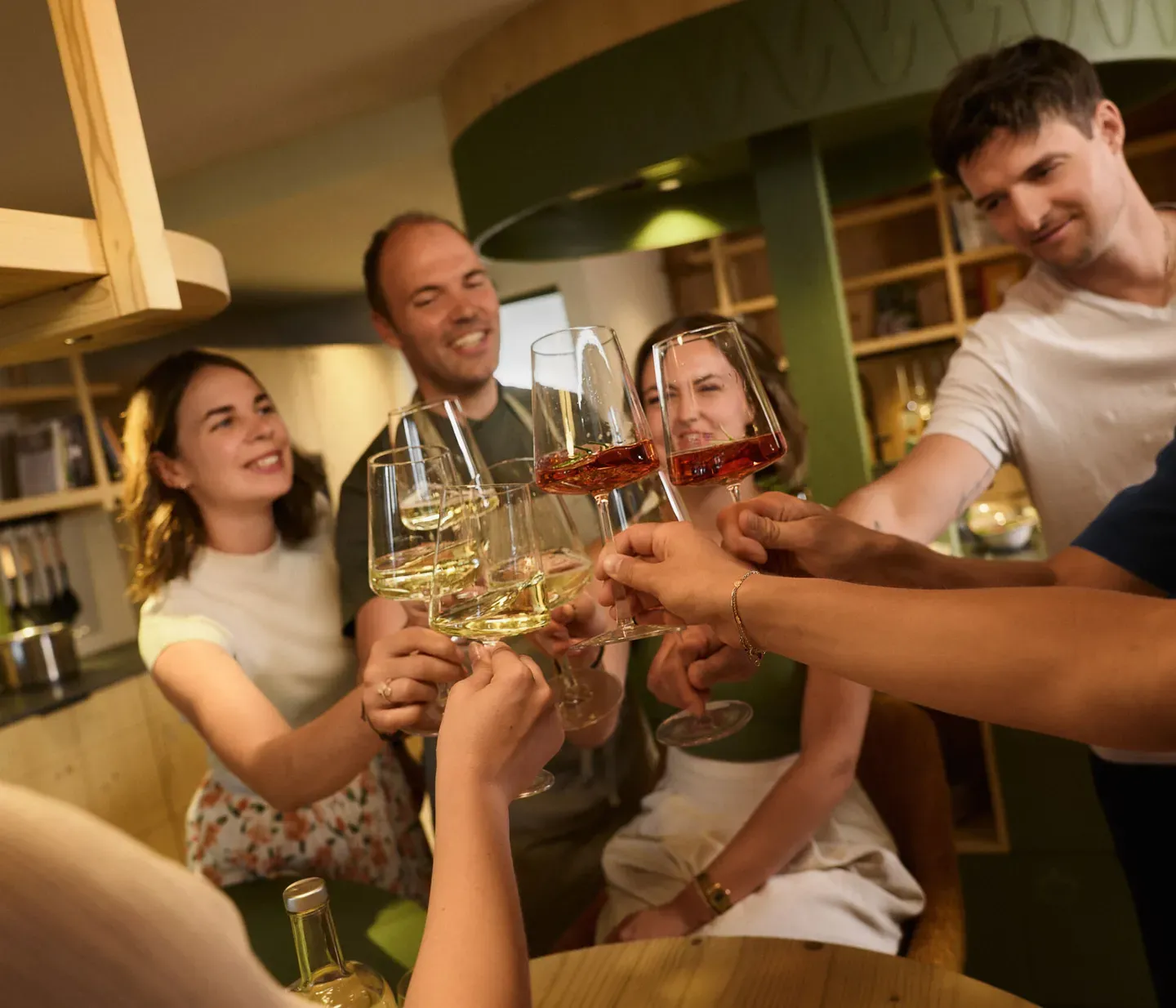 Un gruppo di persone nella cucina conviviale dell’Hotel AUI brinda con calici di vino, festeggiando insieme.