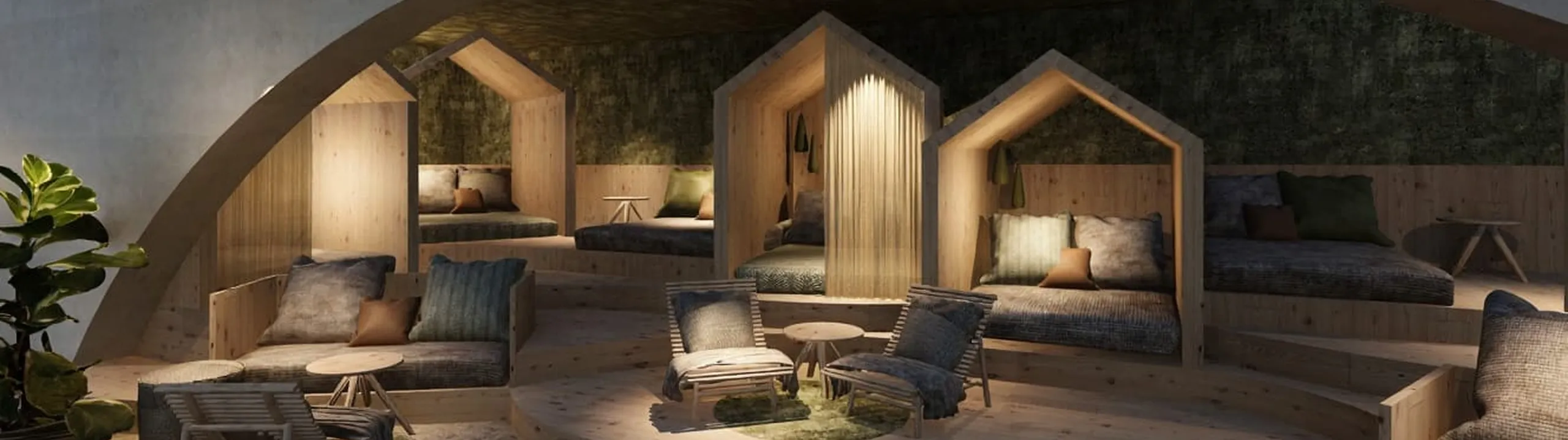 Accogliente area lounge con sedute imbottite all’interno di nicchie in legno a forma di casetta. Illuminazione calda, tavolini rotondi e piante creano un’atmosfera rilassante.