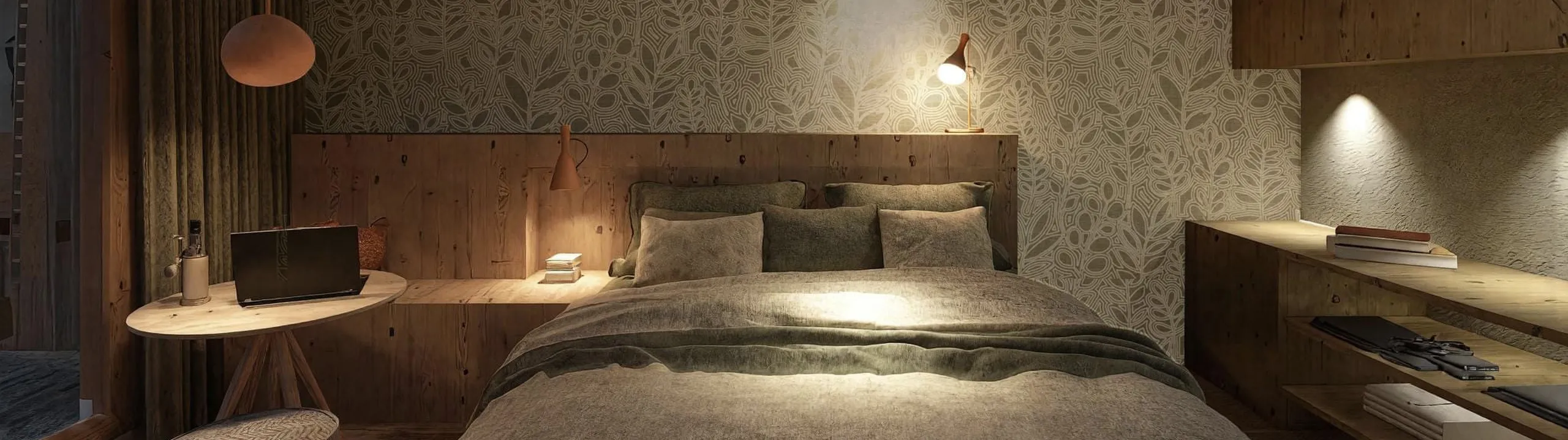 Cozy bedroom with a floral accent wall, soft lighting, and wooden furniture. A bed with gray bedding, laptop on a small table, and ambient warmth.