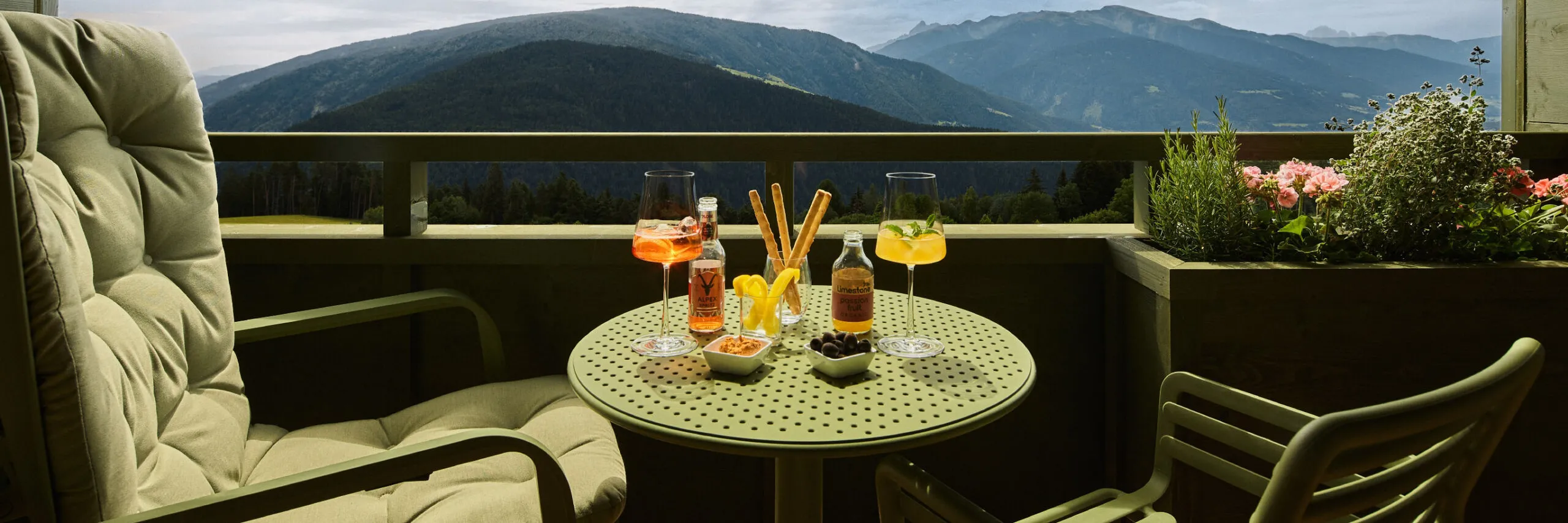 Balcone di una camera AUI con tavolo e sedie, affacciato su una catena montuosa durante un aperitivo.