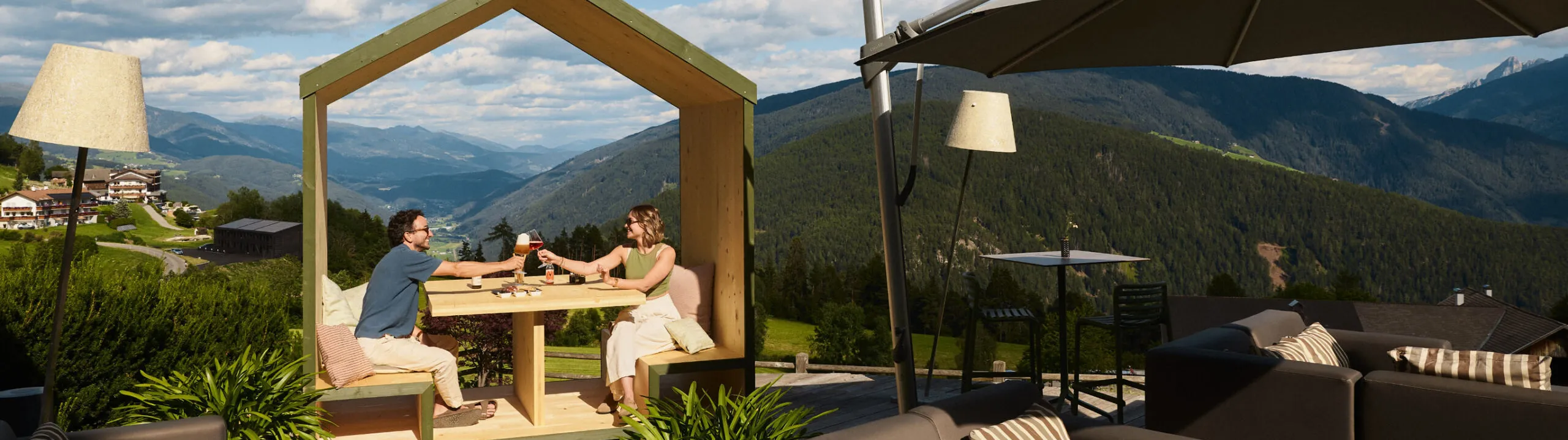 A couple seated on the patio of AUI hotel in Maranza, enjoying the outdoor ambiance and beautiful surroundings.