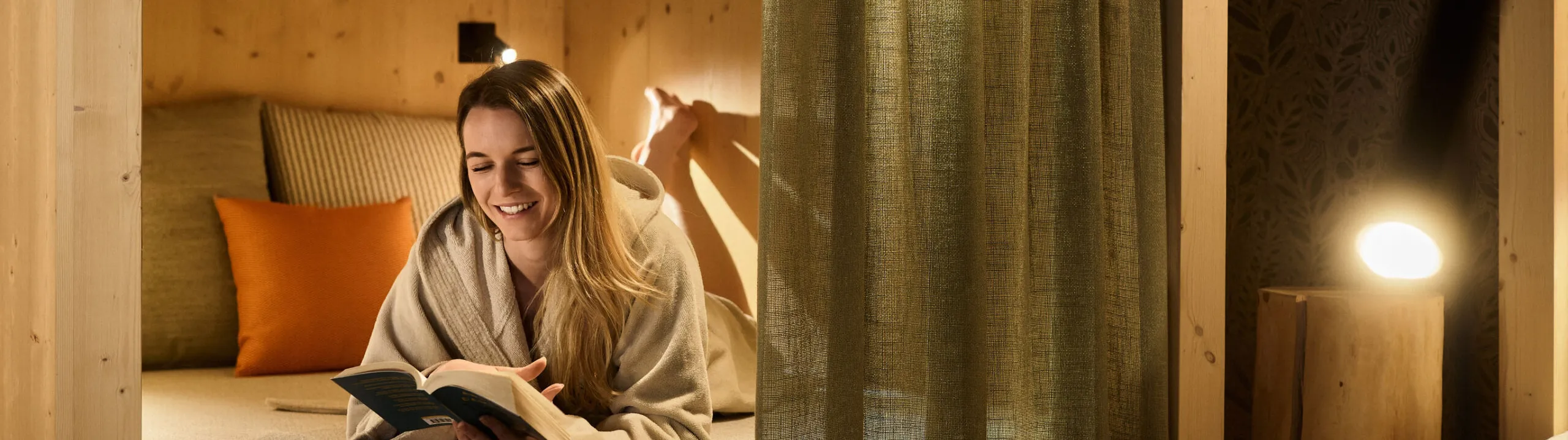 Eine Frau liest gemütlich ein Buch in einem bequemen Bett im ruhigen Wellness-Ruhebereich des AUI Hotels.