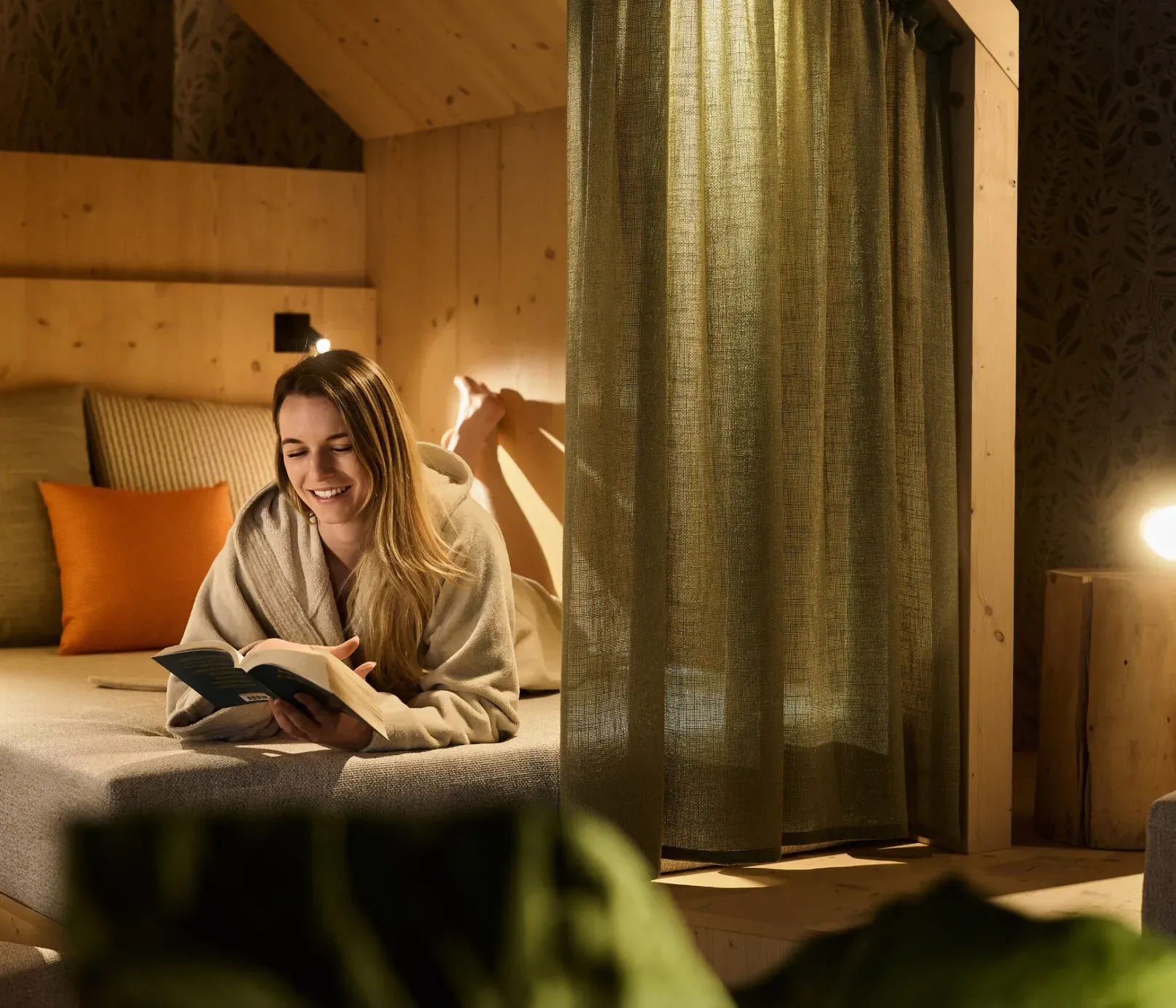 Eine Frau liest gemütlich ein Buch in einem bequemen Bett im ruhigen Wellness-Ruhebereich des AUI Hotels.