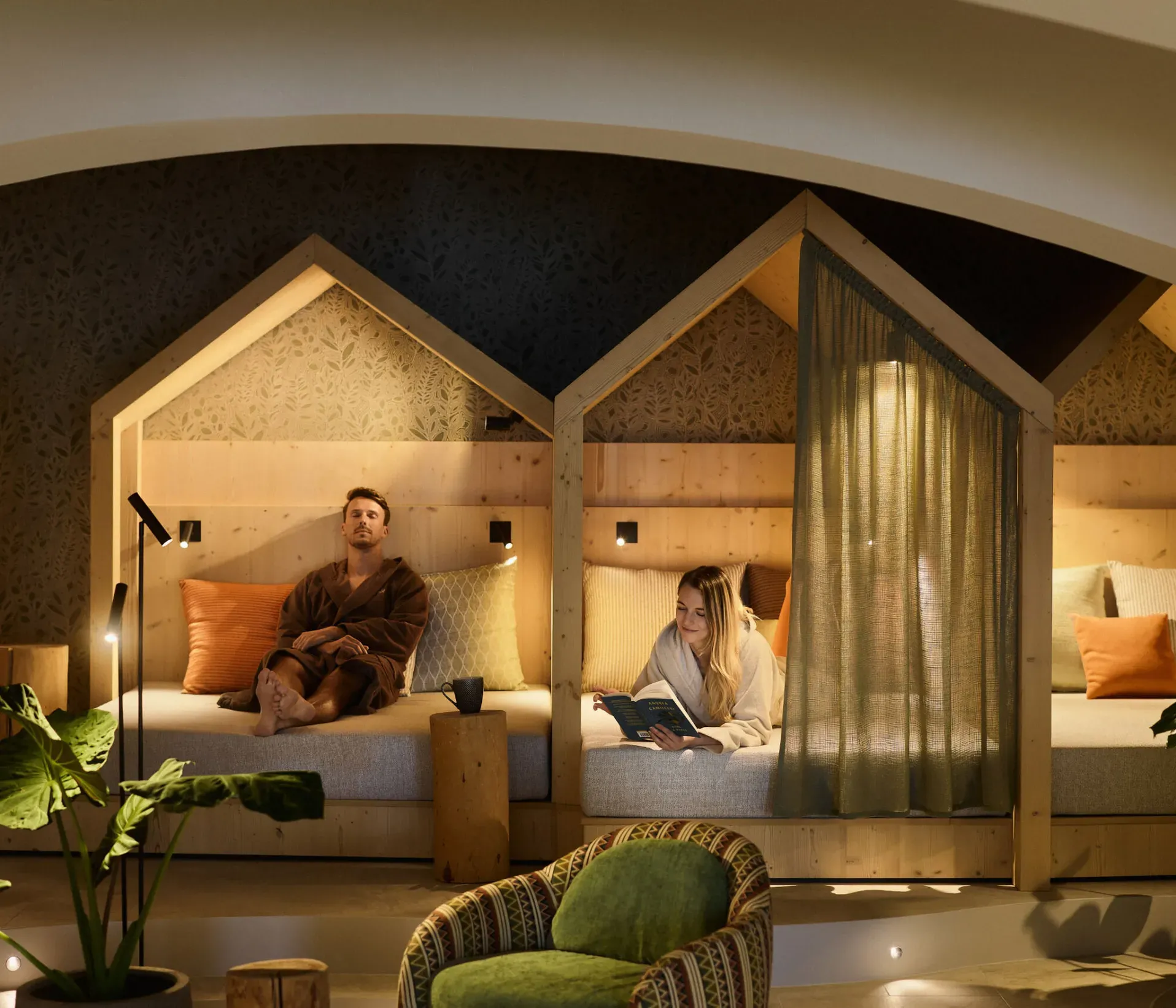 A couple relaxes in the relax room of AUI hotel featuring a bed and a chair, creating a serene atmosphere for relaxation.
