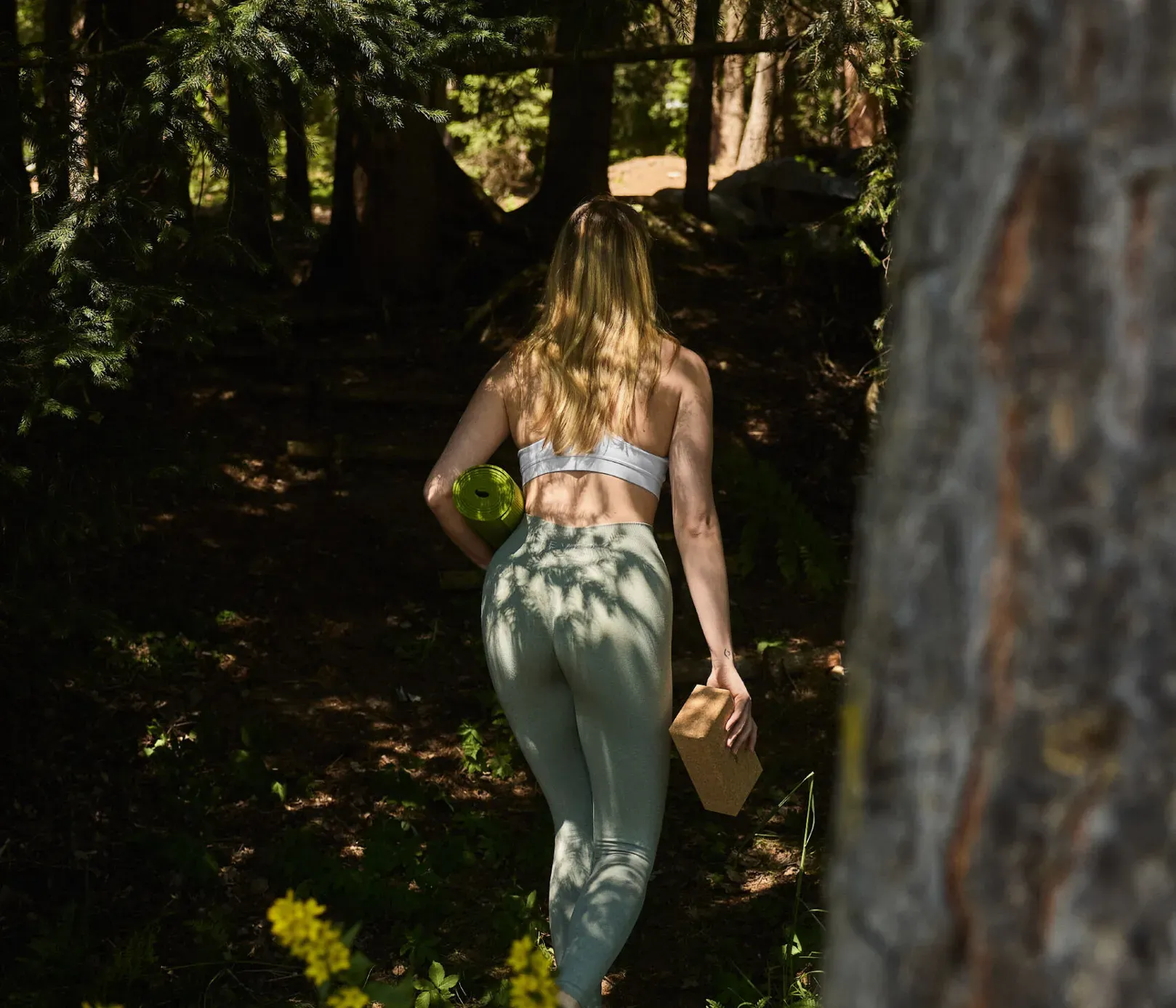 Eine Frau in grünen Leggings geht durch den Garten des AUI Hotels und bereitet sich inmitten der Natur auf eine Yoga-Einheit vor.