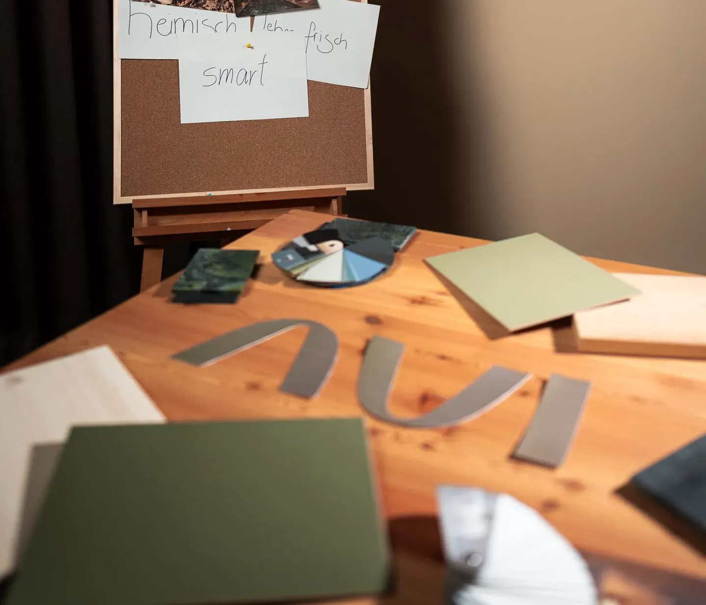 Corkboard on an easel, displaying nature photos, sketches, and notes. A table holds color samples and design materials, suggesting creative planning.